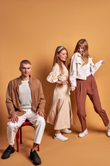 portrait of trendy stylish youth posing at camera isolated on brown background, handsome male and beautiful females in fashionable brown clothes stand together, models