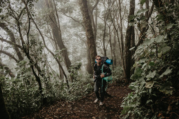 Young man hiking with backpack on in the foggy rainforest