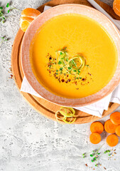 Tasty carrot creamy soup with herbs and spices in a bowl on a grey background top view.  Autumn or winter food. Pureed vegetable soup.