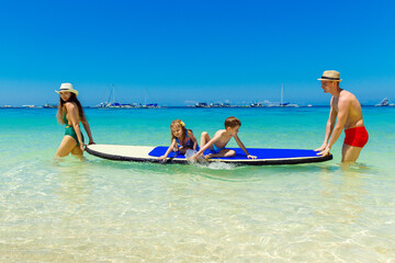 Happy family-mom, dad, little girl and boy have fun on a paddleboard in the tropical sea. The...