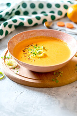 Tasty carrot creamy soup with herbs and spices in a bowl on a grey background. Copy space for text.  Autumn or winter food. Pureed vegetable soup.