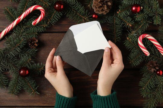 Woman taking blank Christmas card from envelope at wooden table, top view with space for text