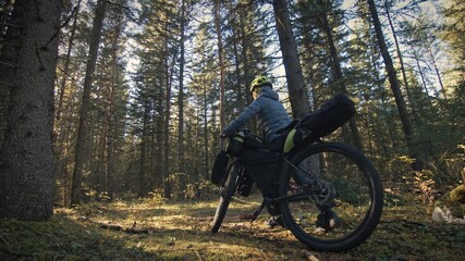 Fototapeta premium The woman travel on mixed terrain cycle touring with bike bikepacking. The traveler journey with bicycle bags. Magic forest park.