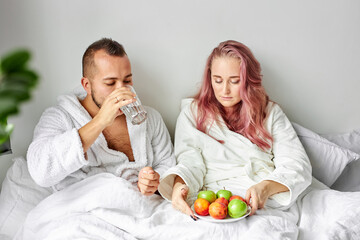 woman give fresh fruits for breakfast to husband, they lie on bed together, have meal, fresh fruits...