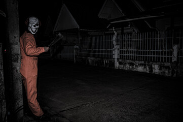Obraz na płótnie Canvas Asian handsome man wear clown mask with weapon at the night scene,Halloween festival concept,Horror scary photo of a killer in orange cloth