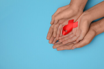 Woman and girl holding red ribbon on blue background, top view with space for text. AIDS disease awareness