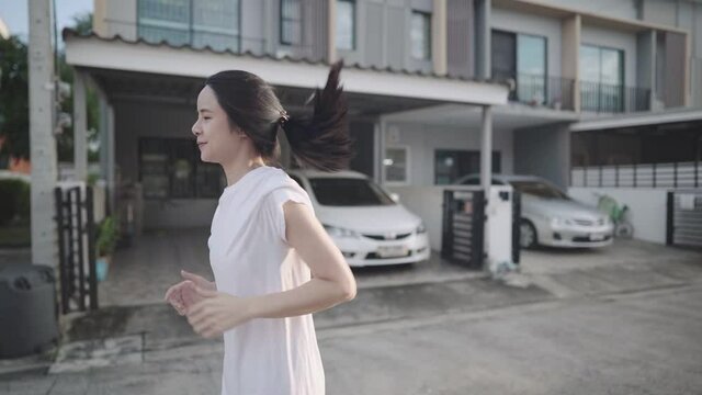 Pretty young asian woman wear white shirt running around house neighborhood passing by houses and parked cars, having fun and joyful moments, fitness motivation body conditioning, relaxing exercise, 