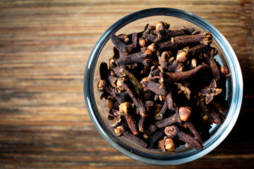 Dried cloves in a bowl over wooden background. Spice clove for favouring.