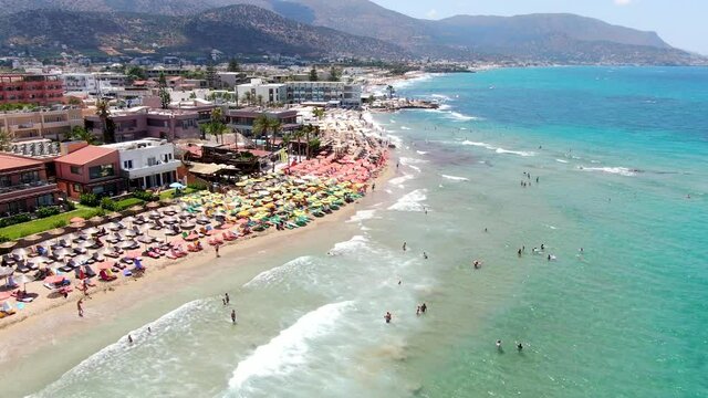 beach world famous as a surfer's paradise. Deck chairs. Ocean surf and waves. Stone cliffs. Aerial view. Greece, Crete, Malia.