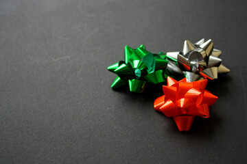 Festive shiny green, orange and silver gift bows for a present wrapping. Black background. Party decorations. New Year 2021. Christmas. Birthday.