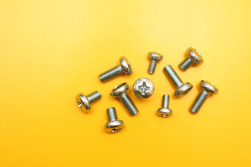 Metal drywall screws on a yellow background, top view, cross screw cap