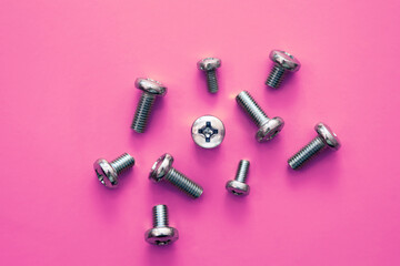 Metal drywall screws on pink background, top view, cross screw cap