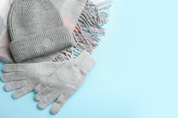 Stylish gloves, scarf and hat on light blue background, flat lay. Space for text