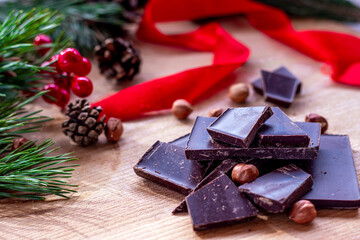 Home made chocolate with Christmas decoration on background. Chocolate, nuts, fir cones and branch, red berries and wrapping tape.  