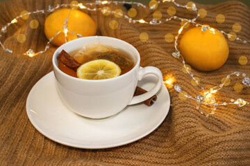 On a warm yellow background, there is a white Cup of tea with lemon and cinnamon next to lemons and bokeh.