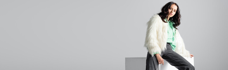  young woman in faux fur jacket posing on cube on white background, banner