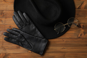 Fototapeta premium Stylish black leather gloves, hat and glasses on wooden table, flat lay