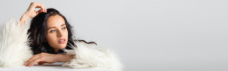  brunette young woman in faux fur jacket posing near cube on white background, banner