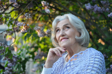 Senior beautiful happy woman posing by lilacs in park