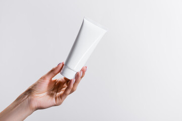 cropped view of woman holding tube of hand cream isolated on grey, stock image