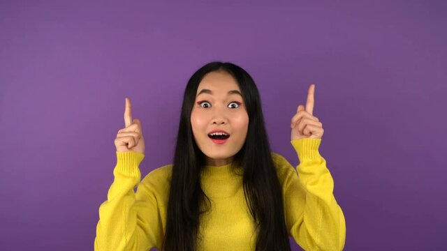 young asian woman on isolated purple background shows up index finger. Free space for object or text 4K