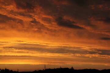 red and yellow sky, with the setting sun, waves of flaming clouds and dark shadows of trees and forests in the background