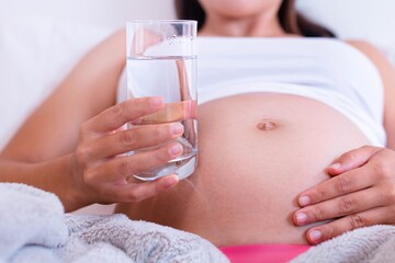 A pregnant woman drinking a glass of water. Maternity health and hydration.