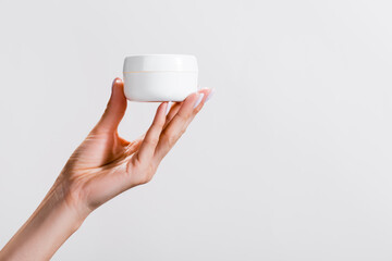 cropped view of woman holding container of hand cream isolated on grey, stock image