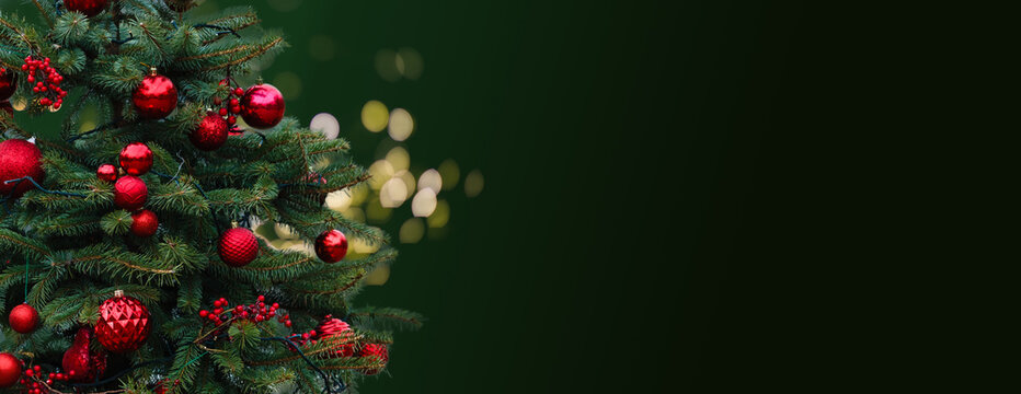 Closeup of Festively Decorated Outdoor Christmas tree with bright red balls on blurred sparkling fairy background. Defocused garland lights, Bokeh effect