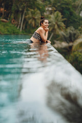 Woman sititng by the swimming pool. Lady in a swimsuit. Girl relaxing by the pool at a beach club in Bali Indonesia