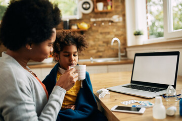 African American mother giving a cup of tea to her ill daughter at home