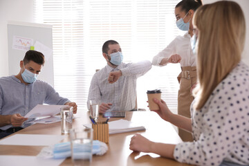 Obraz premium Coworkers with protective masks making elbow bump in office. Informal greeting during COVID-19 pandemic