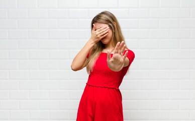 blonde woman covering face with hand and putting other hand up front to stop camera, refusing...