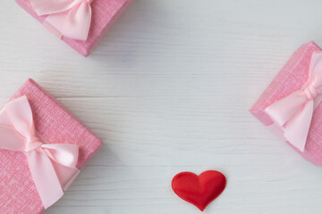 Boxes for small gifts in pastel colors and red satin hearts on a light background with a place for text. Advertising, poster.