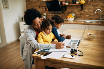 Black single mother taking notes and working while babysitting her kids at home.
