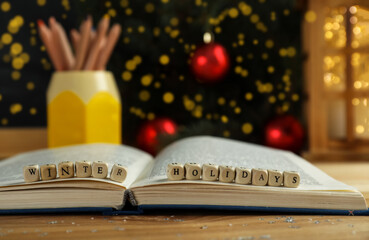 Wooden cubes with phrase Winter Holidays and open book on table, closeup. Space for text