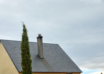 Chimney on a slate tile roof next to a cypress
