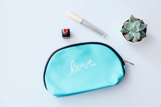 Stylish cosmetic bag, listick, lip gloss and succulent on white table background, top view