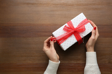 Woman holding white Christmas gift box at wooden table, top view. Space for text
