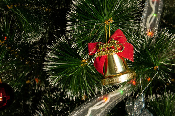 A Christmas tree toy in the form of golden bells with a red ribbon tied in a bow, hanging from a dark green artificial Christmas tree. New Year. Christmas. copy space. horizontal. close-up.