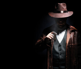 Photo of a shaded detective in jacket and hat holding and smoking cigar on black background.