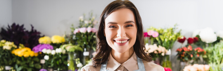 Portrait of happy florist looking at camera with blurred range of flowers on background, banner