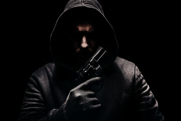 Photo of a creepy horror criminal in black hoodie holding revolver gun. - obrazy, fototapety, plakaty