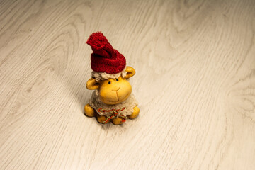 Fototapeta premium a small toy in the form of a smiling white lamb in a red Christmas hat on a light gray laminate. minimalistic. horizontal. New Year. Christmas. vintage. close up. copy space. home decoration.