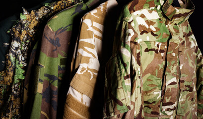 Photo of a hanging military camouflaged jackets on black background. © breakermaximus