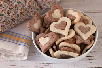 Shortbread cookies of two colors in a white plate on a wooden background. Sweet cookies in the form of hearts for February 14 (Valentine's Day)