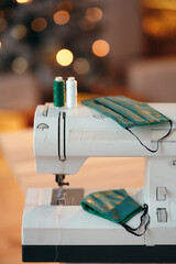 A close-up of sewing threads, sewing machine and handmade Christmas designed cotton face masks. Christmas DIY and handmade concept