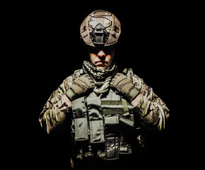 Photo of a fully equipped shaded soldier in armor vest and helmet standing on black background.