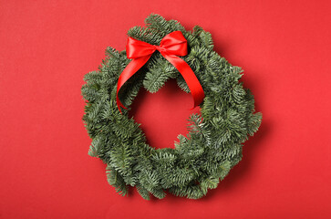 Christmas wreath made of fir tree branches with ribbon on red background © New Africa