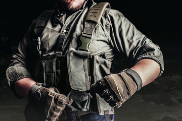 Soldier in tactical outfit and gloves putting on protective armor vest.